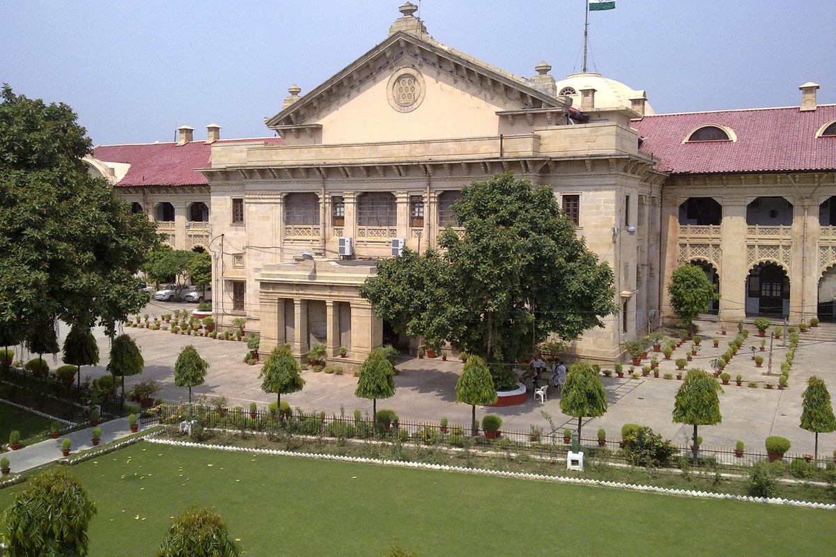 The sandstone main building of the Allahabad High Court with a red tiled roof, a domed tower and the Indian flag, seen across a lawn.