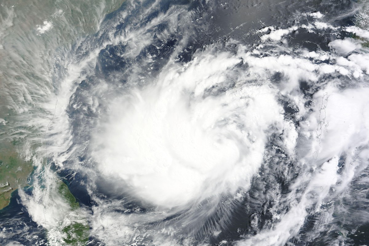 Satellite view of a large white spiral of cloud over the dark blue Bay of Bengal, with the Indian coastline at the left edge.