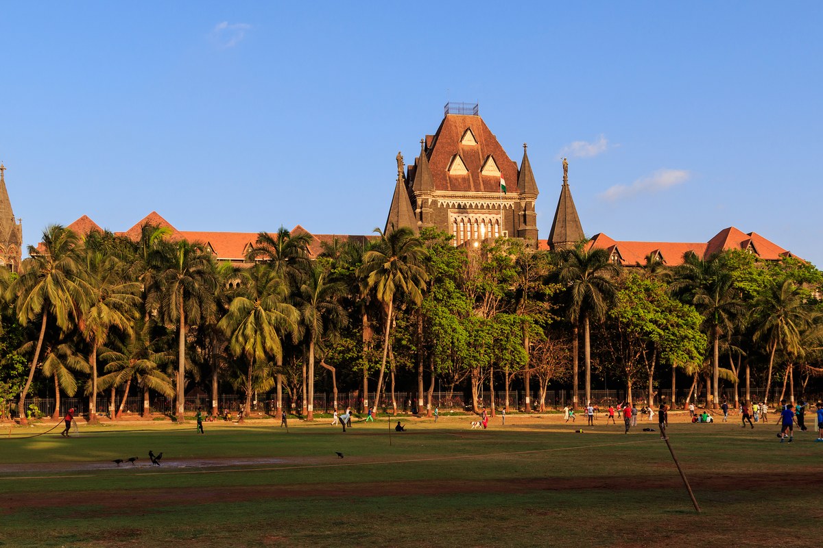 The Bombay High Court’s Gothic Revival building with its central tower, seen across the Oval Maidan lined with palm trees in Mumbai.