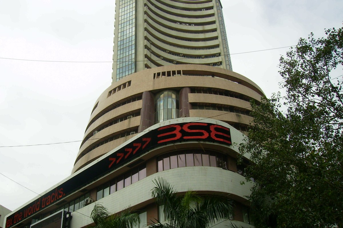The curved tower of the Bombay Stock Exchange building in Mumbai with its red BSE sign, seen from street level among trees.