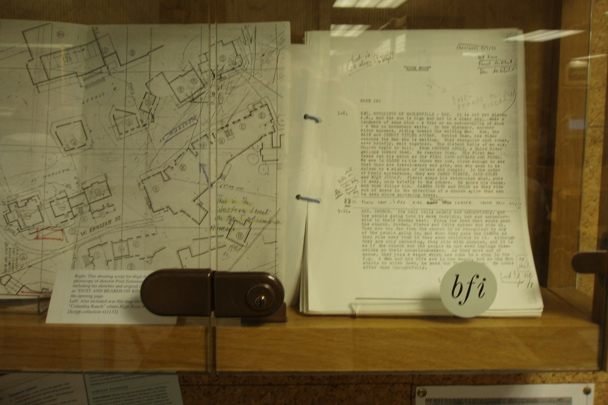A typed, hand-annotated film shooting script and a hand-drawn set map displayed side by side in a glass case at a film library.