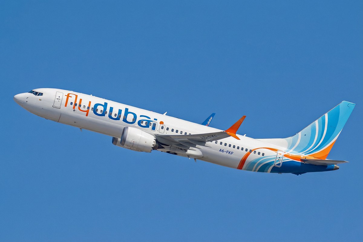 A white flydubai Boeing 737 MAX with blue and orange livery climbing against a clear blue sky.