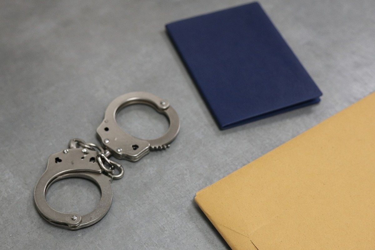 A pair of steel handcuffs on a grey desk beside a plain dark blue passport and a brown envelope, in an AI-generated representative scene.