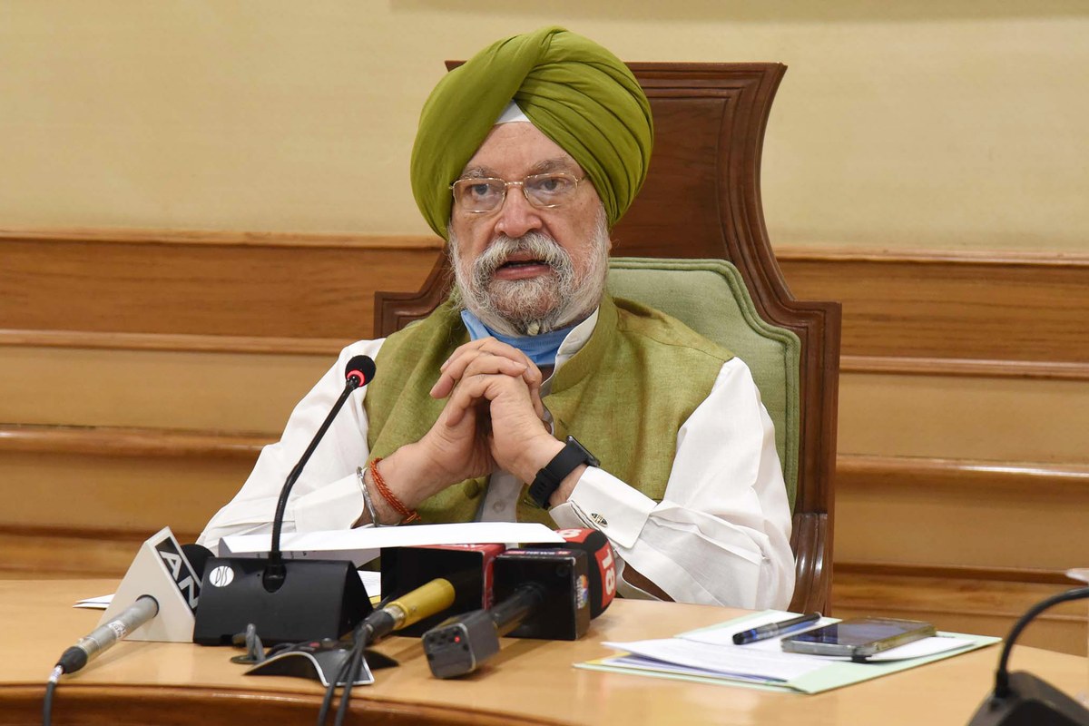 Hardeep Singh Puri, in a green turban and waistcoat, speaks at a press conference in New Delhi, seated behind a row of news microphones.