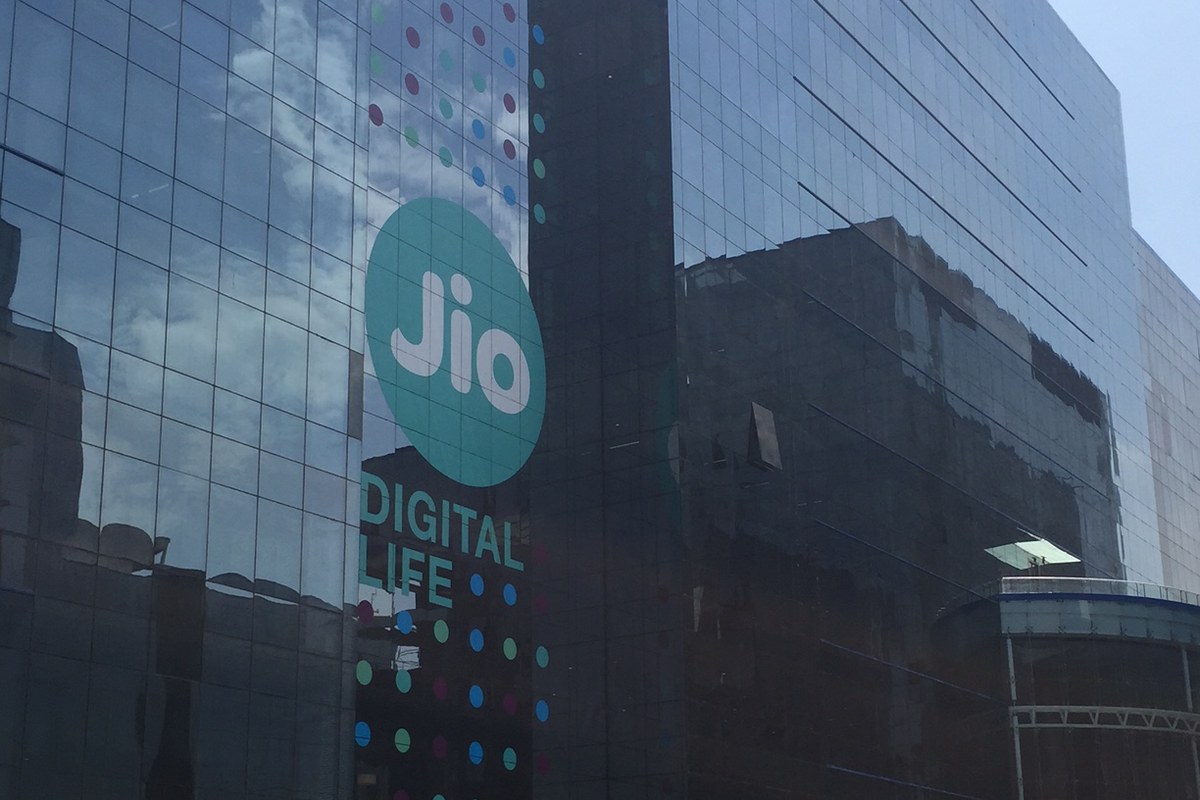 Glass office building with a large teal Jio logo and the words Digital Life on its facade, under a blue sky.