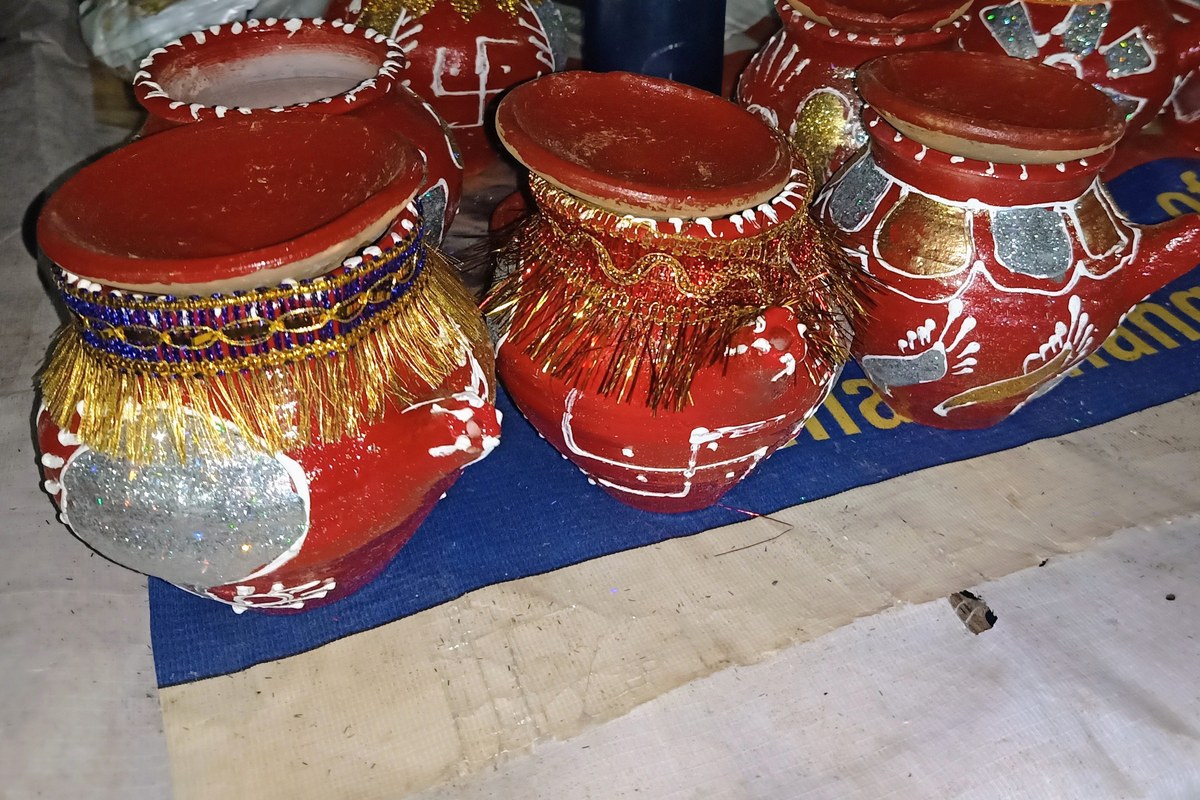 Red clay karwa pots decorated with gold tinsel and white patterns, kept for Karwa Chauth puja.
