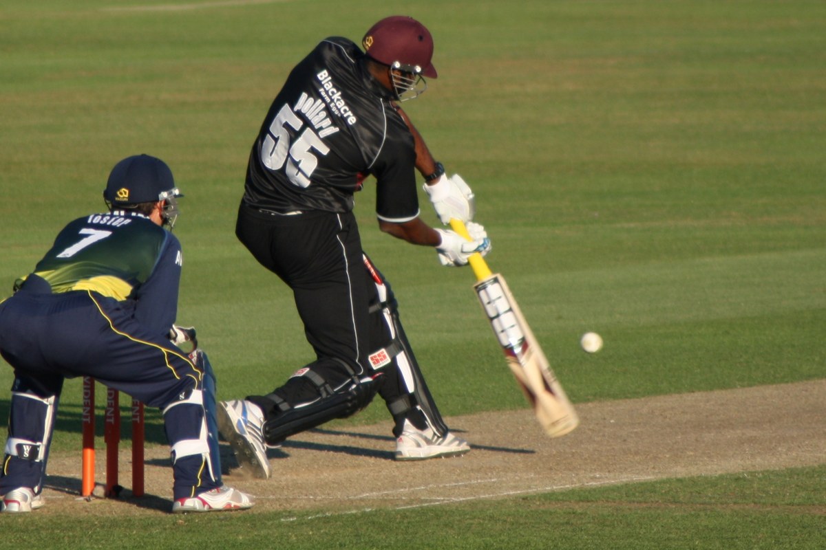 Kieron Pollard, in a black kit with the number 55 and a maroon helmet, plays a shot as the wicketkeeper crouches behind the stumps.