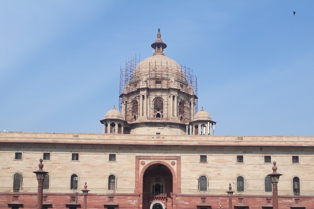 The red and cream sandstone North Block building on Raisina Hill with its central dome, under a clear blue sky.