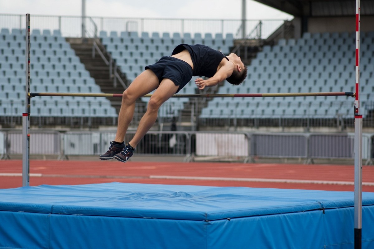 An anonymous athlete arches backwards over a high-jump bar above a blue landing mat in an empty stadium, in an AI-generated representative scene.