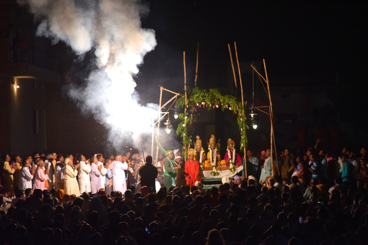 Night-time Ramnagar Ramlila scene with costumed performers beneath a decorated arch and spectators gathered around them.