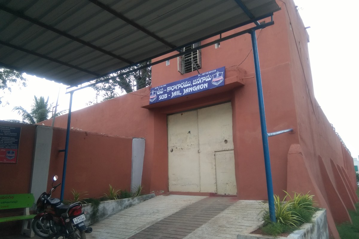 The closed cream-coloured gate of a sub-jail set in a red-painted wall, with a blue name board above it and a metal canopy over the entrance.