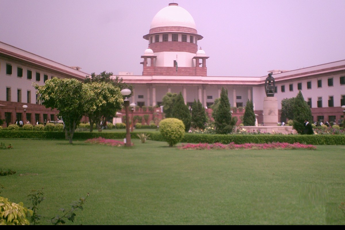 The Supreme Court of India building in New Delhi, with its central dome, behind a lawn, trees and a statue.