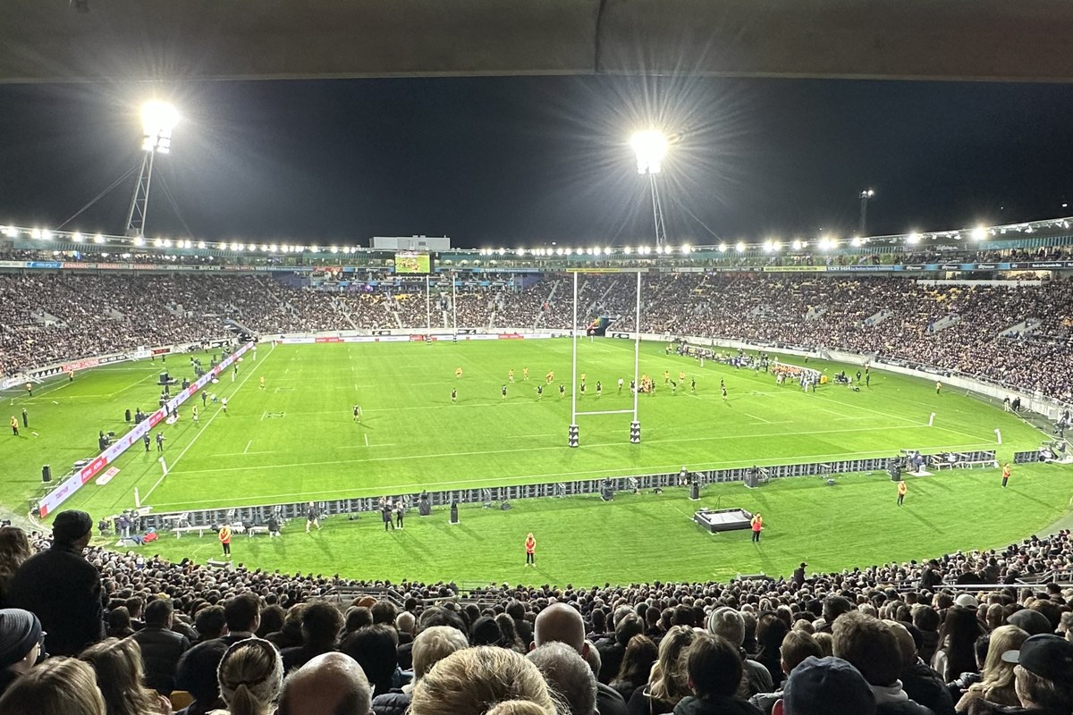 A packed stadium in Wellington under floodlights at night, seen from the stands, with a green field and rugby goalposts.